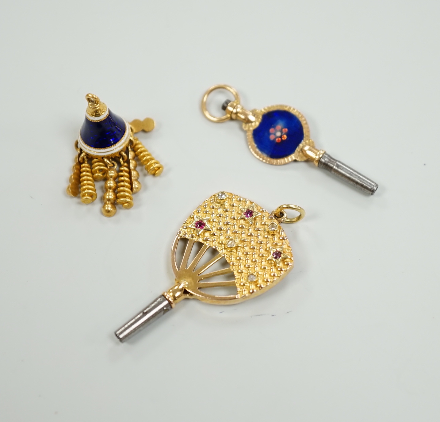An early 20th century yellow metal (stamped 15), ruby and diamond set watch key, 39mm, together with a three colour enamelled watch key and an enamelled tassel charm.
